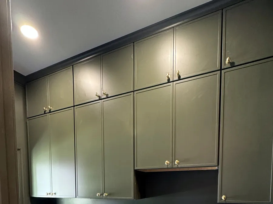 Painted green cabinetry running to the ceiling with brass knobs